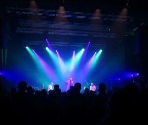 Le chanteur Thomas Breinert sur la scène du Tangram à Évreux, éclairé par des lumières bleues et violettes, devant les silhouettes du public